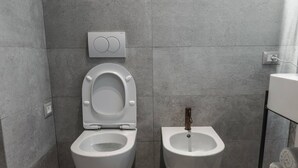 Een moderne badkamer met toilet en bidet, betegelde wanden en een zichtbaar stopcontact.