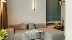 Een moderne woonkamer met een grijze bank, een kleine ronde tafel en een eethoek met een gele stoel.