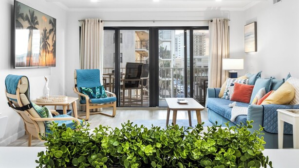 A modern living room with a sofa, chairs, a coffee table, and a balcony with a city view. - Gorgeous Cocoa Beach Condo: Balcony, Heated Pool, BBQ Grills & Hot Tub ☀️ (Cocoa Beach)