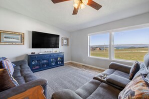A living room with a sectional sofa, a flat-screen TV, a blue cabinet, and large windows with a view. - A Scenic Custer Getaway with Space, Comfort, & View of the Needles (Custer)