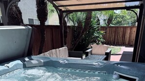 A hot tub with a pergola overhead, surrounded by a wooden fence and potted plants.