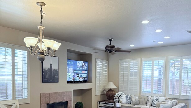 A spacious living area with a dining table, white chairs, a sofa, a TV mounted on the wall, and a ceiling fan.
