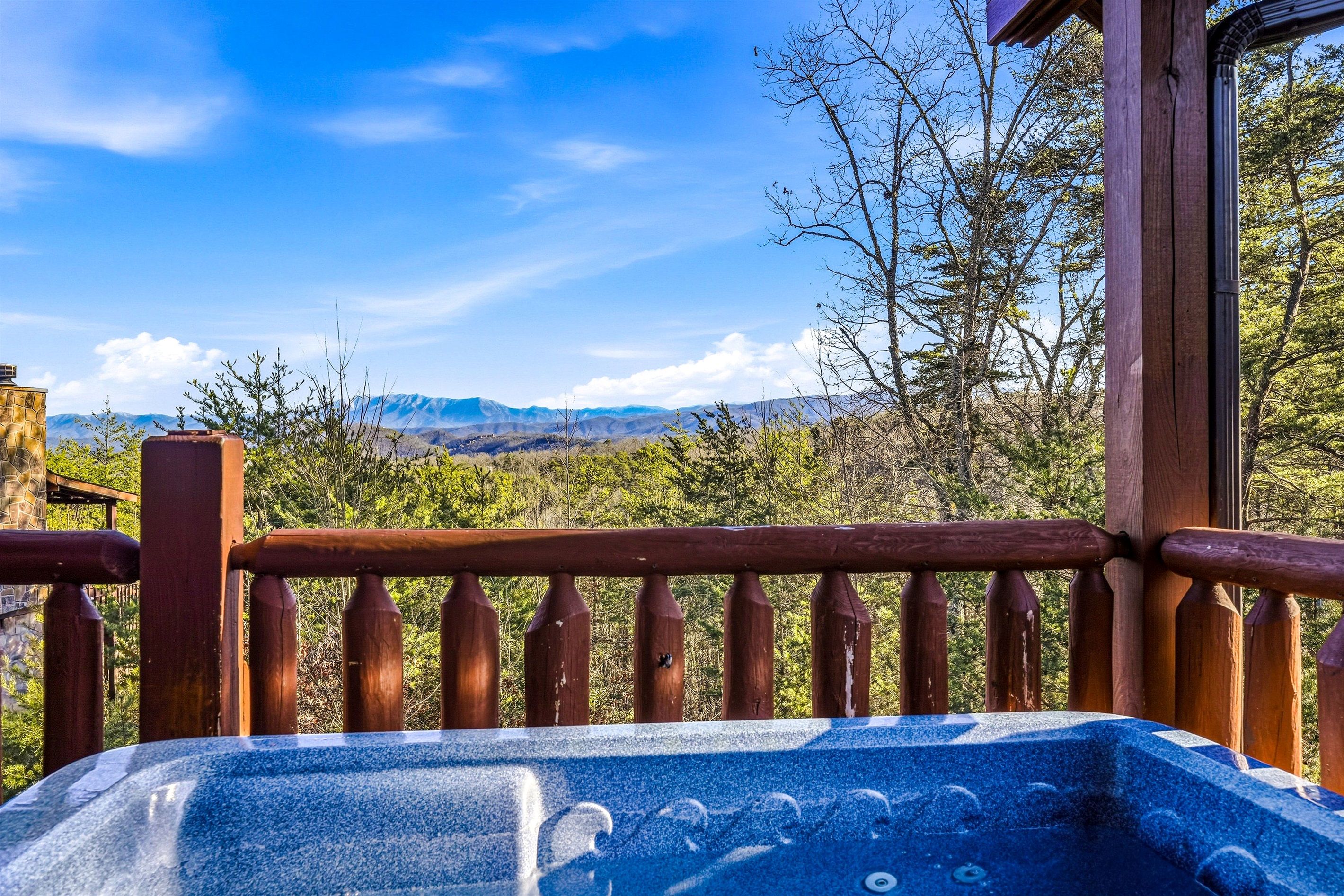 A hot tub on a wooden deck with a view of mountains and trees.