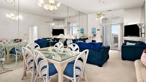 Ein modernes Wohnzimmer mit einem Glastisch, weißen Korbstühlen, einem blauen Sofa und einem Deckenventilator.