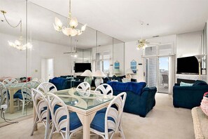 Ein modernes Wohnzimmer mit einem Glastisch, weißen Korbstühlen, einem blauen Sofa und einem Deckenventilator.