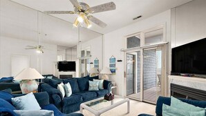 Ein modernes Wohnzimmer mit einem blauen Sofagarnitur, einem Flachbildfernseher, einem Deckenventilator und einem Kamin.