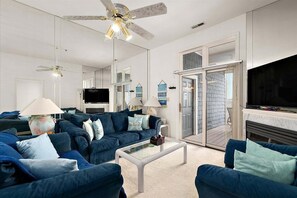 Ein modernes Wohnzimmer mit einem blauen Sofagarnitur, einem Flachbildfernseher, einem Deckenventilator und einem Kamin.