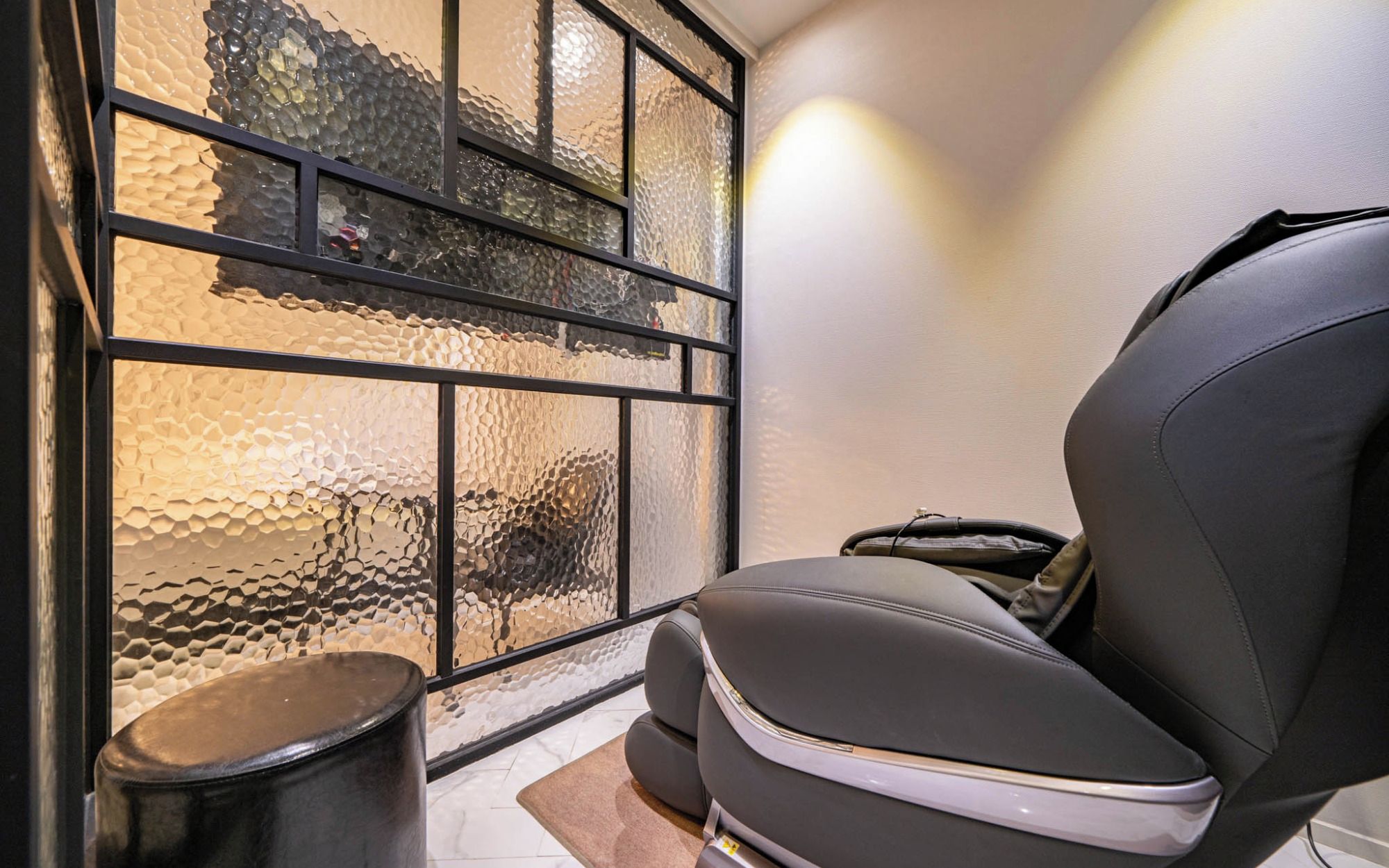 A room with a massage chair, a trash bin, and a window with textured glass.