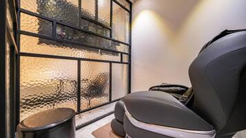 A room with a massage chair, a trash bin, and a window with textured glass.