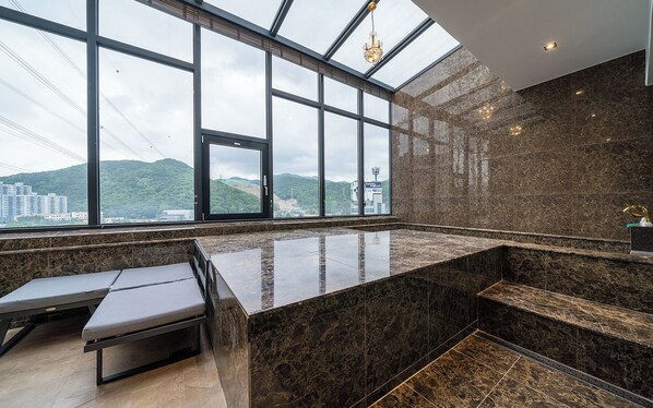 Une salle de bain moderne dotée d’une grande fenêtre, de plans de travail en marbre et d’un banc.
