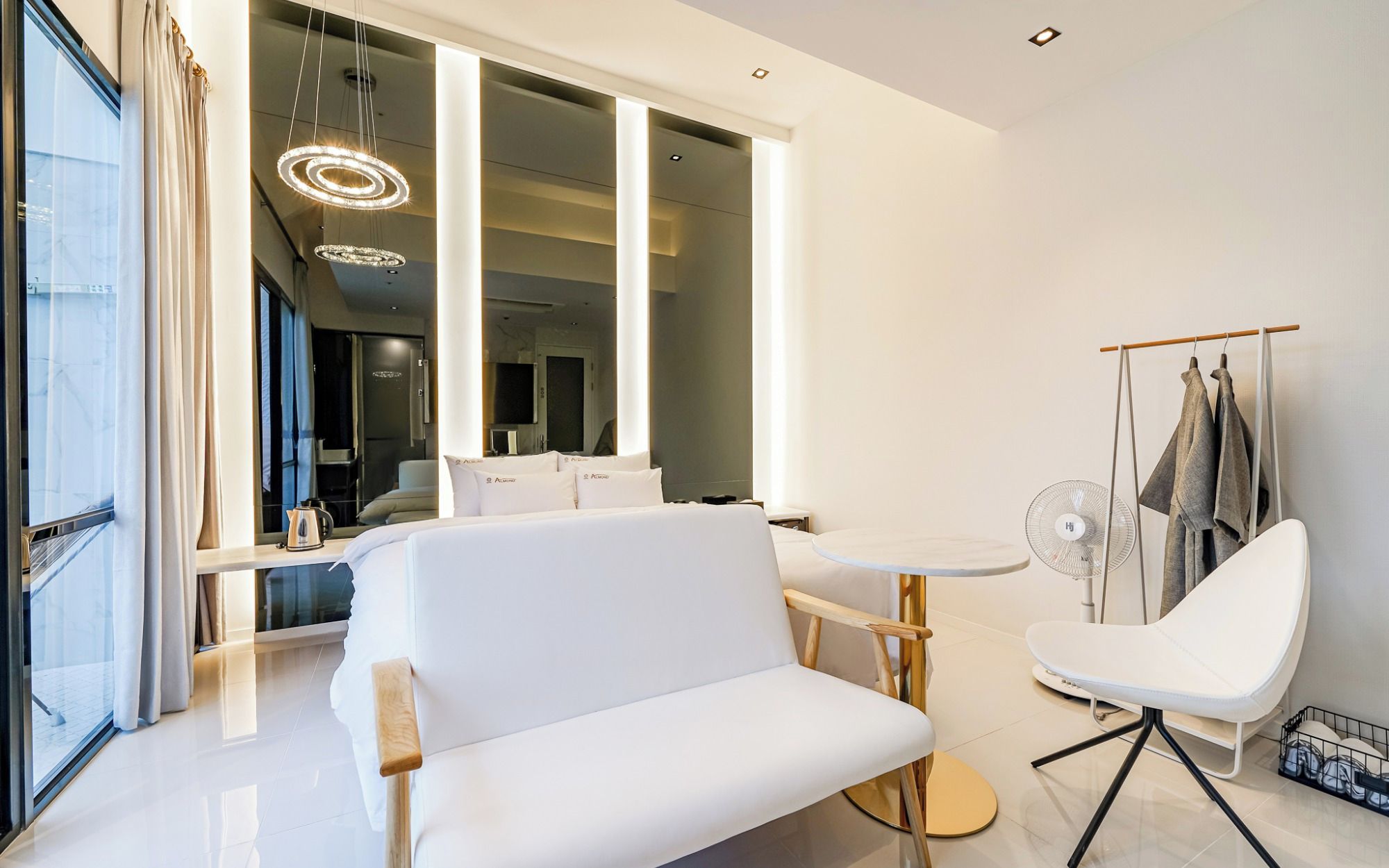 Una habitación de hotel moderna con un ventanal grande, un sofá blanco, una mesa de comedor redonda y una silla.