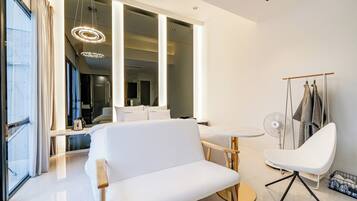 Una habitación de hotel moderna con un ventanal grande, un sofá blanco, una mesa de comedor redonda y una silla.