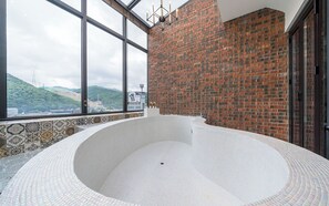 Un bain à remous avec vue sur un mur de briques et une fenêtre donnant sur un paysage vallonné.