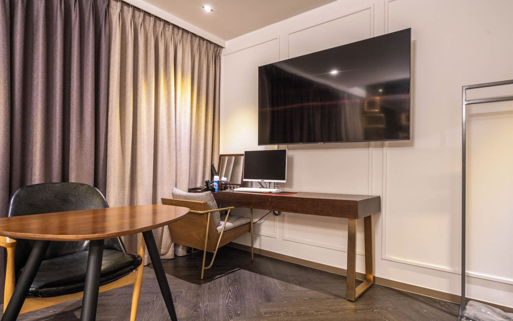 A modern hotel room with a flat-screen TV, a wooden desk, a chair, and a dining table.