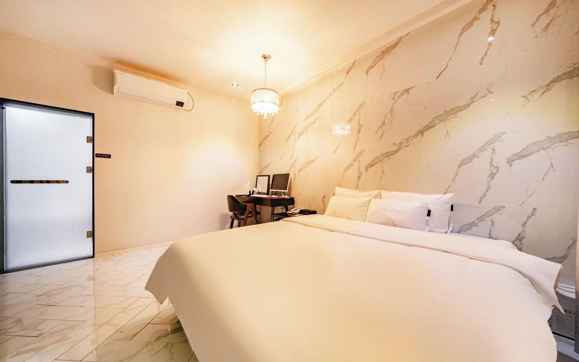 Una habitación de hotel con una cama, un escritorio, una silla, una computadora y un candelabro.