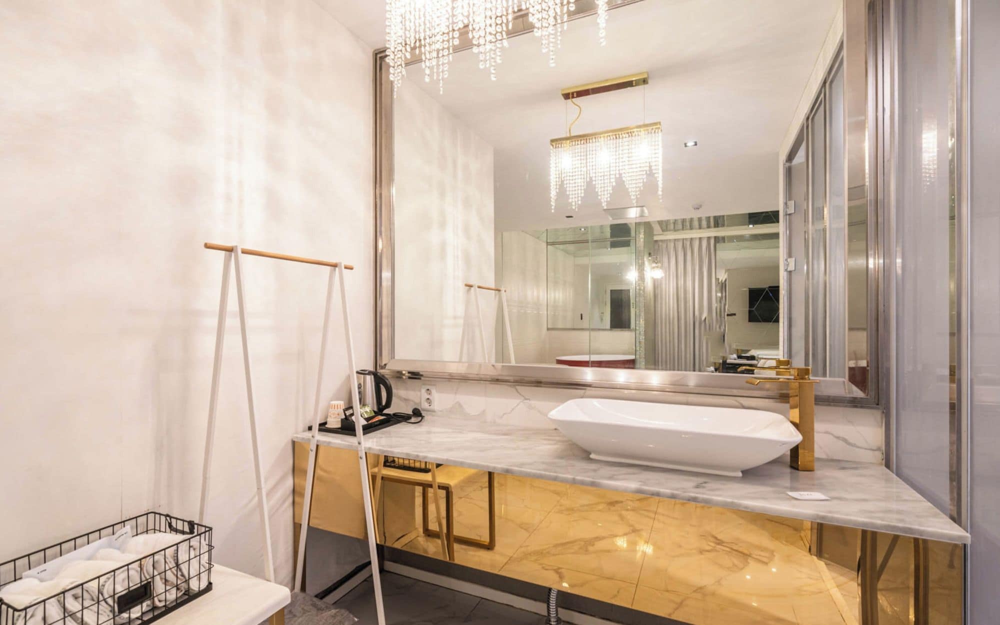 Un baño moderno con un espejo grande, un lavamanos blanco y un mueble de tocador dorado.