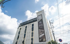 Ein Hotel mit moderner Fassade, ein großes Banner zur Eröffnung und ein Verbotsschild für Parkplätze.