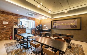 Un hall d’hôtel avec un mur en briques, un comptoir d’accueil et un espace détente avec des tables et des chaises.