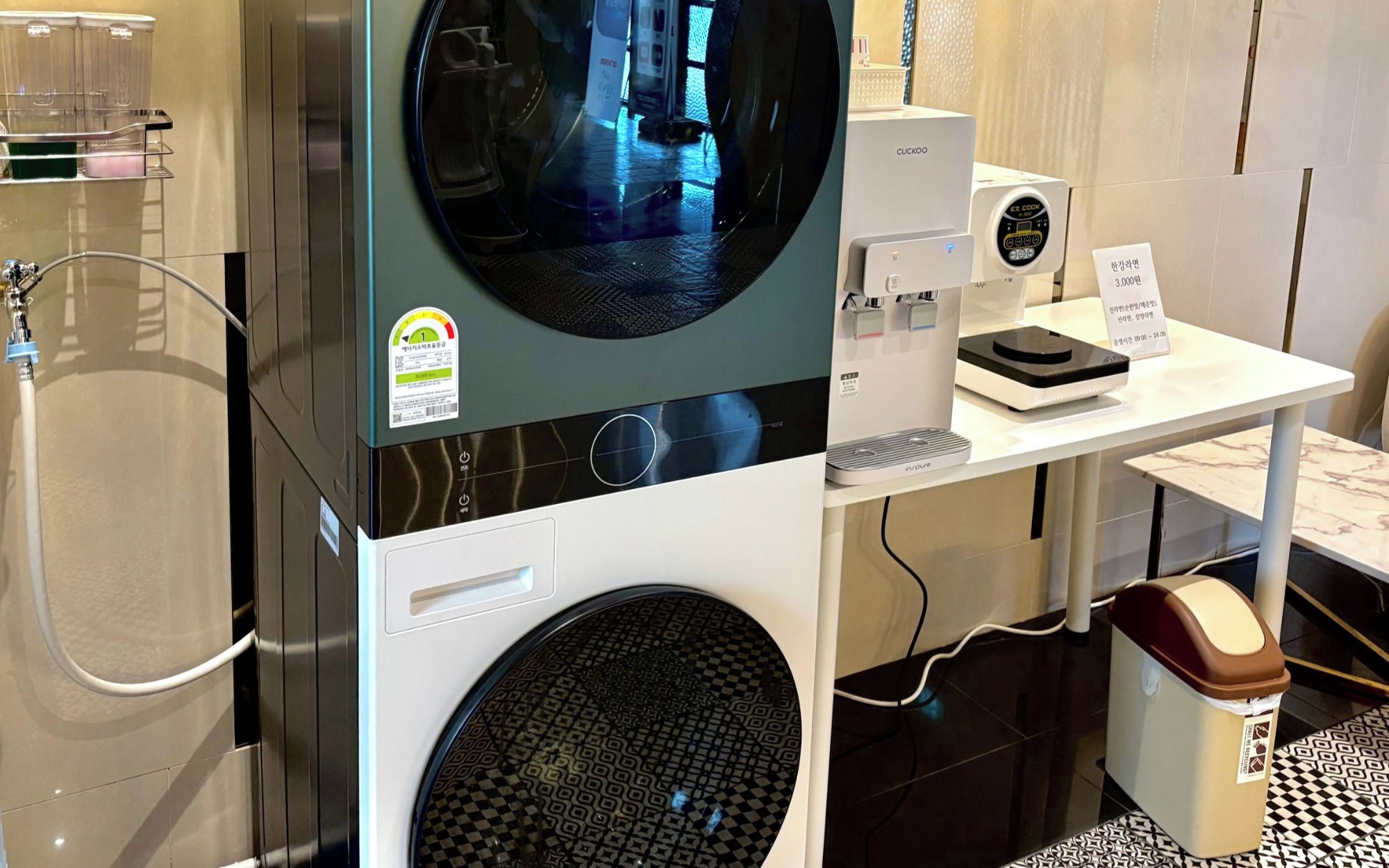 Uma lavanderia moderna com máquina de lavar de carregamento frontal, secadora e uma cafeteira sobre uma mesa.