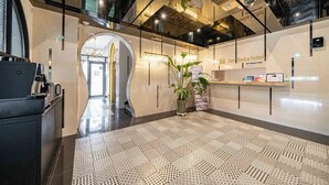Un hall d’hôtel moderne avec un sol à motifs géométriques, un comptoir d’accueil et un grand miroir.