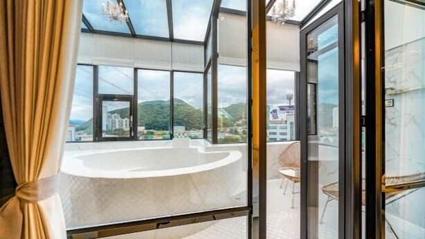 Une salle de bain moderne dotée d’une grande baignoire, d’une douche en verre et offrant une vue sur le paysage urbain et les montagnes.