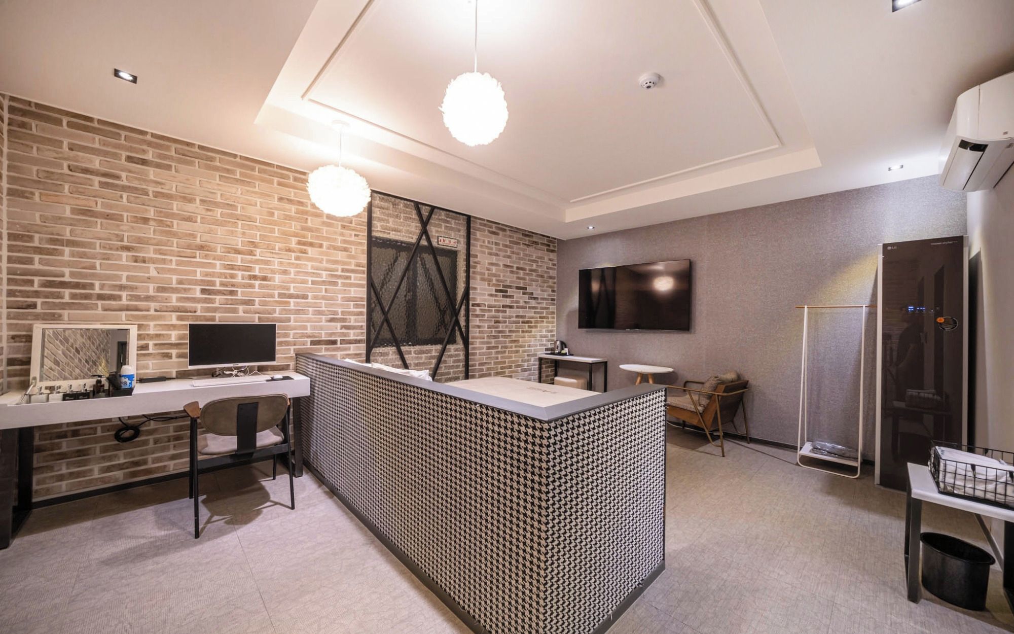 A modern interior with a brick wall, a flat-screen TV, a desk with a computer, and a seating area with a patterned partition.