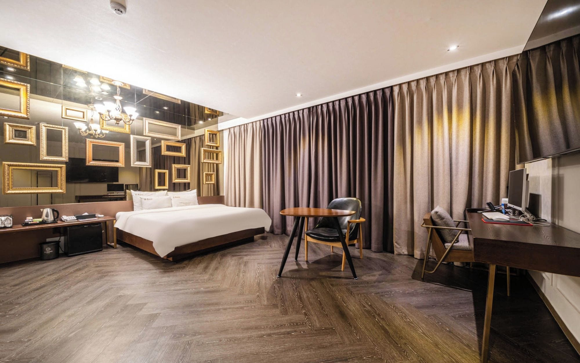 A hotel room with a large bed, a desk with a chair, a television, and a wall with framed mirrors.