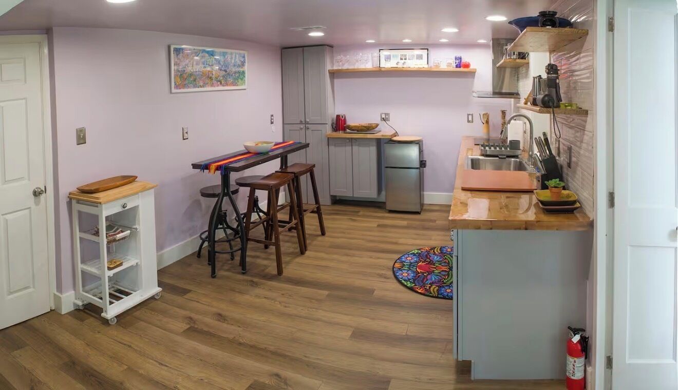 Una cocina compacta con refrigerador, lavamanos y taburetes de madera.