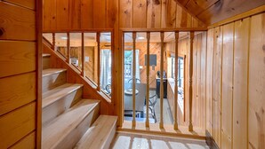 Eine Holztreppe führt zu einem Raum mit Schreibtisch und Stuhl, einem Fenster und Blick ins Freie.
