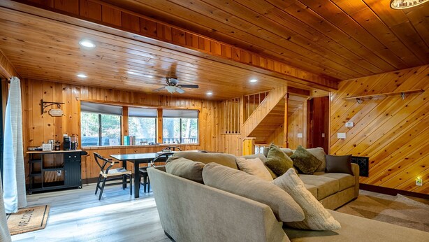 Ein gemütliches Blockhaus-Interieur mit Holzbalkendecke, einer Couch mit Kissen, einem Essbereich und einer Treppe.