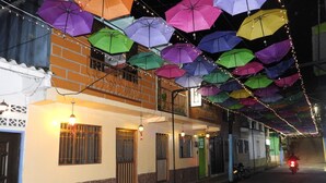 A street with colorful umbrellas hanging overhead, a motorcycle parked on the side, and a building with barred windows and a green door.