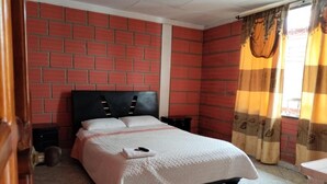 A bedroom with a brick-patterned wall, a bed with a white bedspread, two bedside tables, and a window with striped curtains.