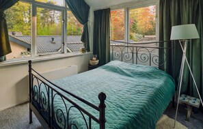 A bedroom with a bed, a nightstand, a lamp, and a view of trees through large windows. - Lovely home in Apeldoorn with WiFi (Apeldoorn)