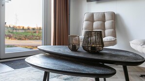 Un saló modern amb una taula rodona, dos vasetes decoratives, un butaquesa amb textura i una vista per una finestra gran.