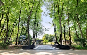 A tree-lined entrance to a residential area with a welcome sign and a sign indicating the name 'Kleine Loo.'