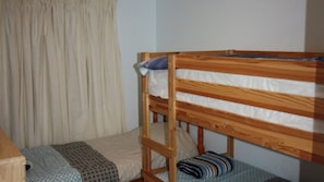 A bunk bed with a wooden frame, a single bed with a patterned blanket, and a curtain. - In Holiday Mode is a basic house in Manyana (Manyana)