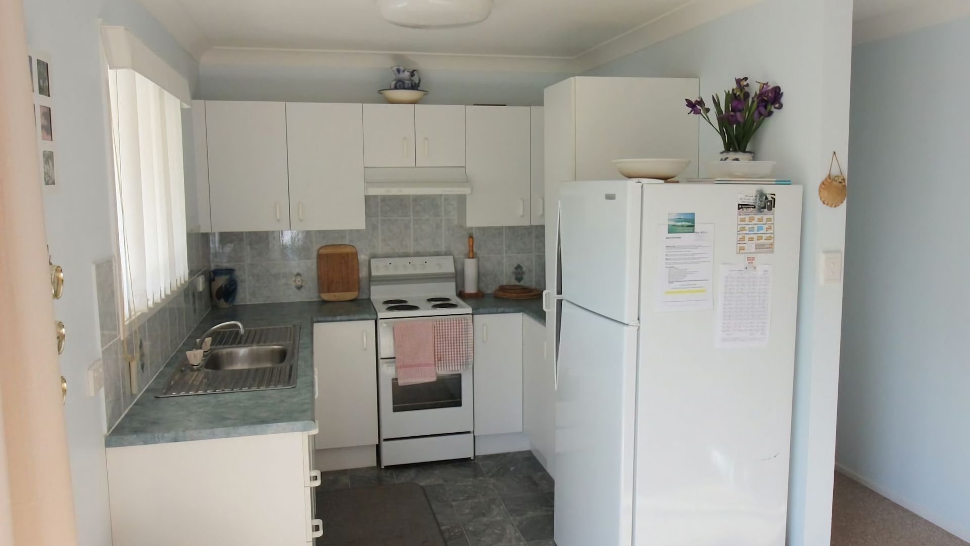 A compact kitchen with white cabinets, a stove, a sink, and a refrigerator.