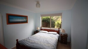 A bedroom with a bed, two bedside tables, a window with a view of greenery, and a framed picture on the wall. - In Holiday Mode is a basic house in Manyana (Manyana)