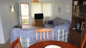 A living room with a sofa, a television, a dining table with chairs, and a bookshelf. - In Holiday Mode is a basic house in Manyana (Manyana)
