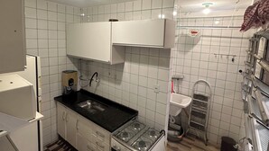 A compact kitchen with white cabinets, a black countertop, a gas stove, and a sink. - Carnival Vacation for 5 people, Praia Grande (Praia Grande)