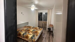 A bedroom with a bed, a ceiling fan, a window with curtains, and a small table with a chair. - Carnival Vacation for 5 people, Praia Grande (Praia Grande)