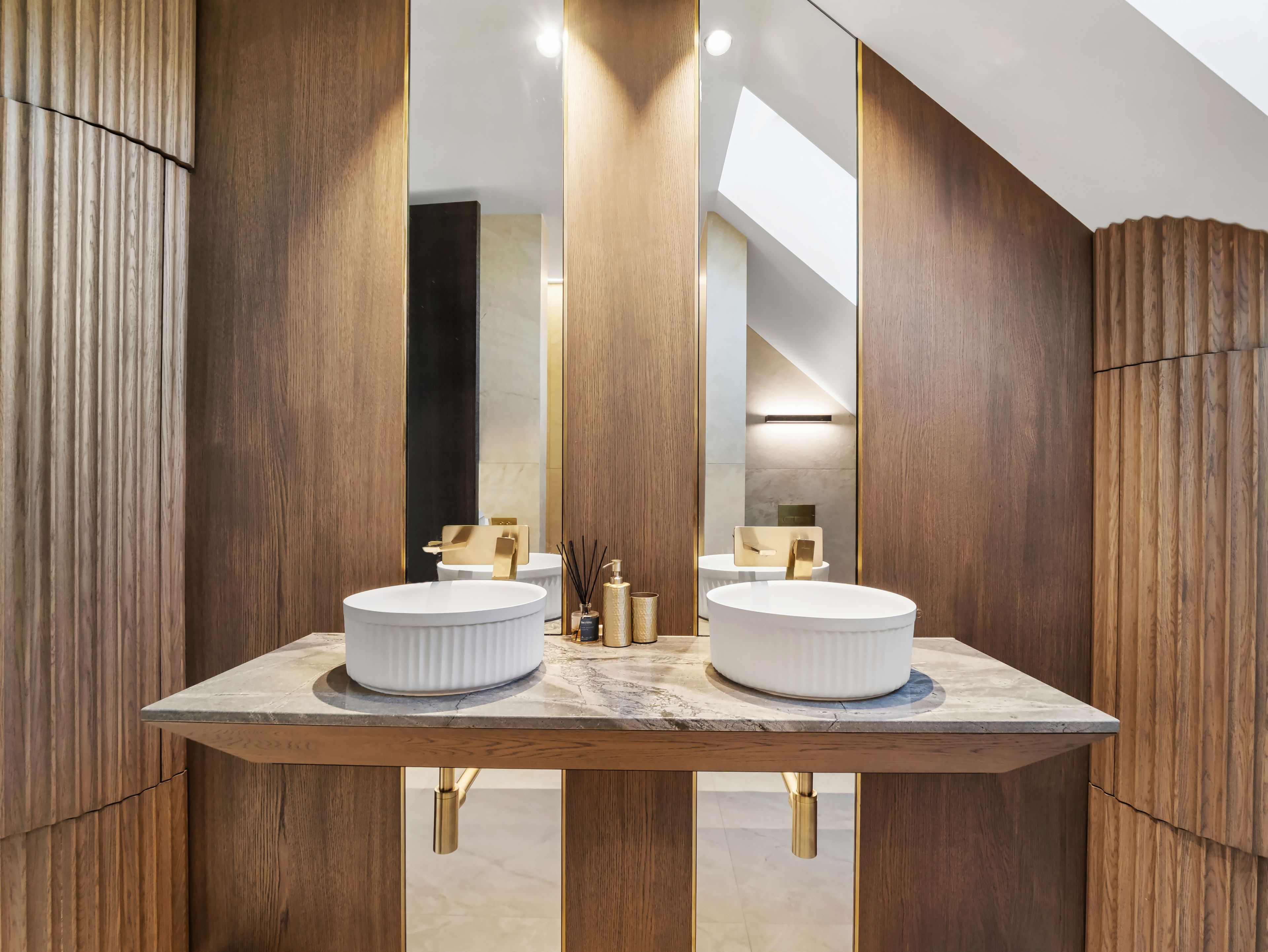 Une salle de bain moderne avec deux vasques, un lambris en bois et un puits de lumière.