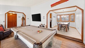 Une table de billard avec une queue de billard, une table à manger avec des chaises et un téléviseur fixé au mur.