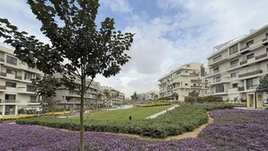 A residential complex with modern architecture, a central lawn, and purple flowering plants. - Chic 2BR Serviced Apartment At Sodic Villette (Cairo Governorate)