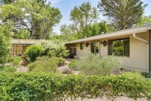 A house with a covered patio area, surrounded by various shrubs and trees.