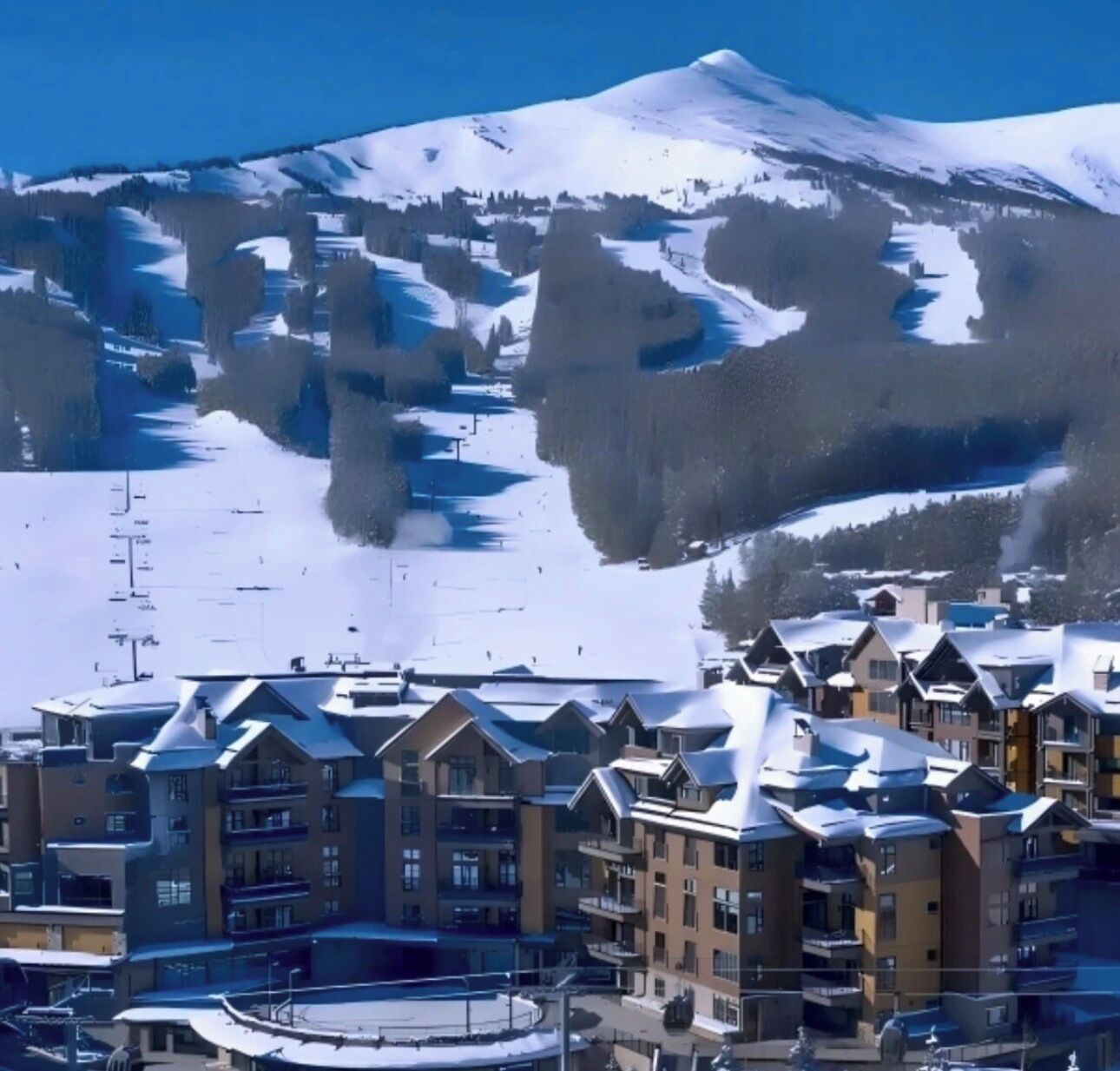 A snow-covered mountain with a ski resort in the background. There are multi-story buildings with balconies in the foreground.