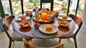 A dining table with breakfast items, a bottle, and a view of a cityscape through large windows. - Amaneceres frente a los volcanes, piso 18. Bright space with open city views (Heroica Puebla de Zaragoza)