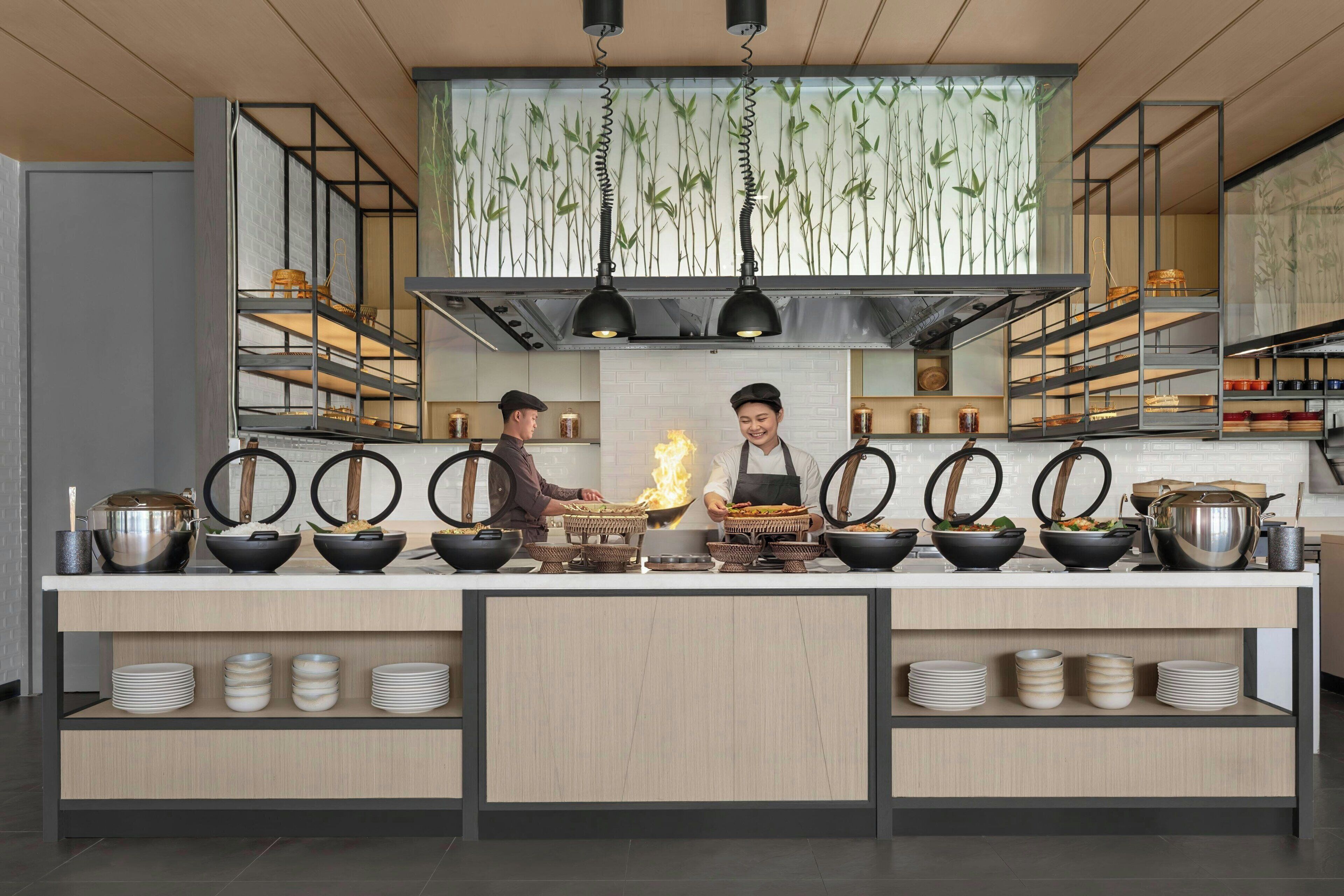 Una cucina moderna con due chef al lavoro, scaffali con pentole e utensili, e una parete a tema bambù.