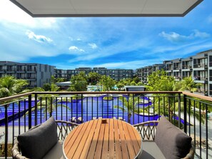 A balcony with a wooden table and chairs, overlooking a swimming pool and modern buildings. - Courtyard By Marriott Phuket Chalong Bay Resort (Chalong)