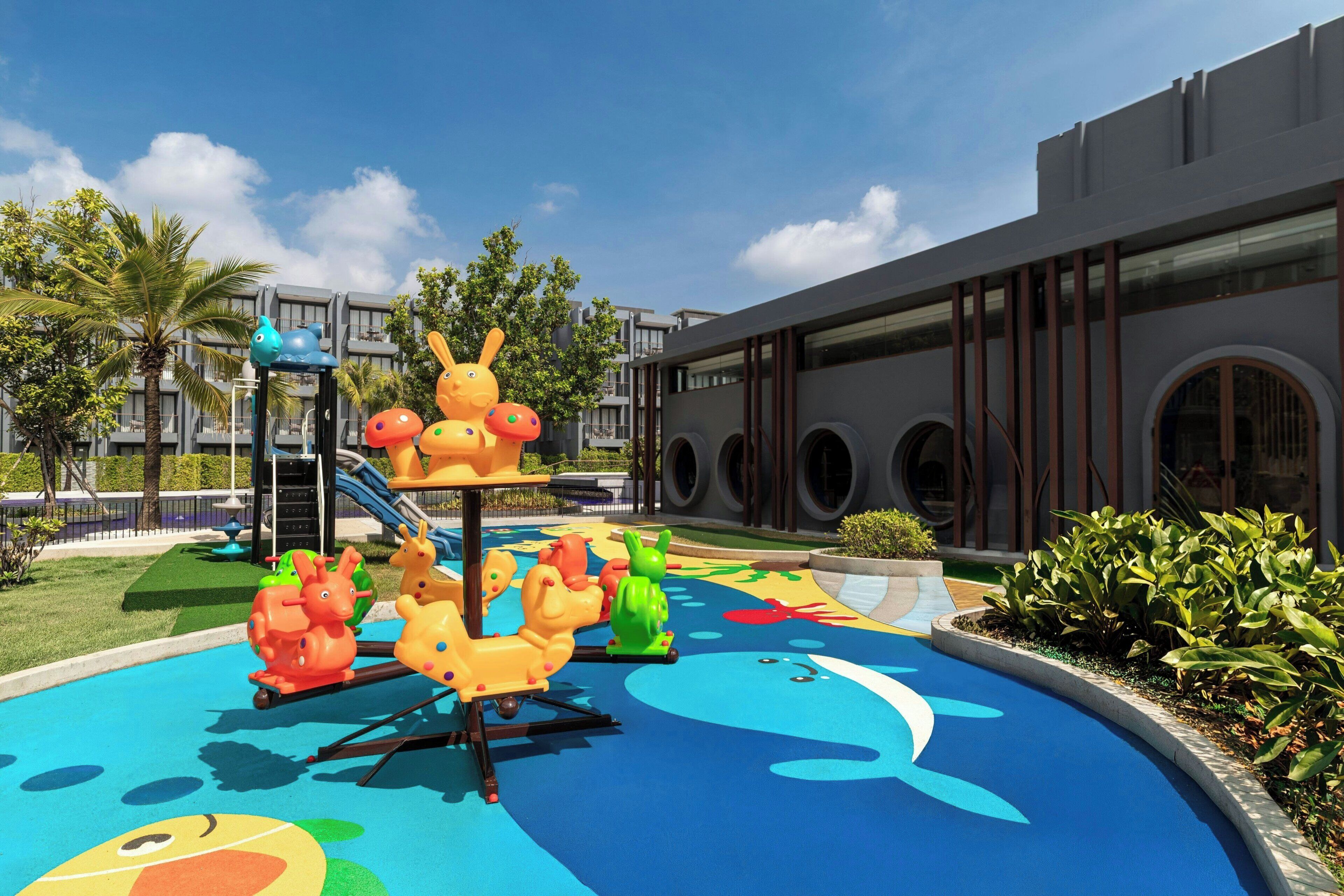 A playground with colorful animal-shaped rides and a building with large windows and a modern design.